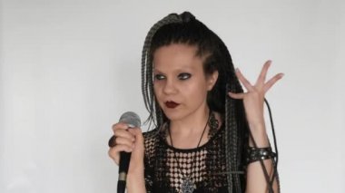 Uzun gri afro örgülü, koyu renk makyajlı gotik bir kız mikrofonla şarkı söylüyor. O bir vokalist veya şarkıcı gibi davranıyor. Müzik malzemeleri mağazası için yaratıcı bir konsept..