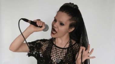 Uzun gri afro örgülü, koyu renk makyajlı gotik bir kız mikrofonla şarkı söylüyor. O bir vokalist veya şarkıcı gibi davranıyor. Müzik malzemeleri mağazası için yaratıcı bir konsept..