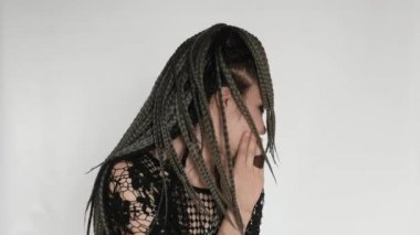 An unusual gothic girl with long afro braids and a dark make up slapps her face, smiles, laughs and says something. A creative concept for cosmetics, afro hairstyle haidresser's or a fashion company.