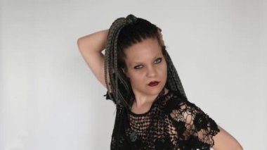 A gothic girl with long afro braids and a dark make up moves along the music, dances and strokes her hair.  A creative concept for cosmetics, afro hairstyle haidresser's or a fashion company.