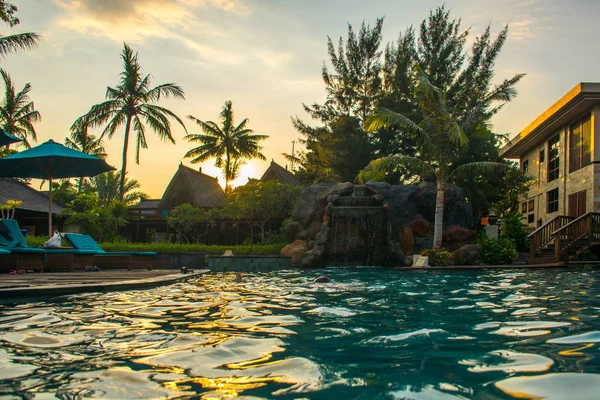 Tumbonas en la playa cerca de la piscina en el complejo tropical con palmeras durante la puesta del sol, Gili Trawangan, Lombok, Indonesia —  Fotos de Stock