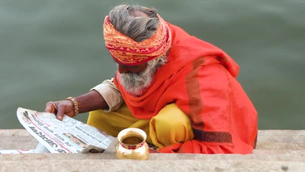 VARANASI INDIA, 10 MAR 2019 - Sadhu ou Santo sentado e lendo jornal nas Gats perto do rio Ganga, vídeo de filmagem 4k — Vídeo de Stock