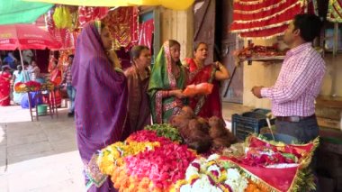 India, Varanasi, Mar 10 2019 - Man with women threading and negotiating colourful flower garlands and hindu offers for the gods near Ganga River, 4k footage video