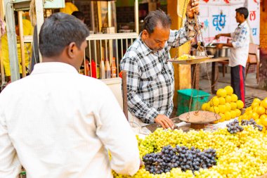 Hindistan, Varanasi, Mar 10 2019-tanımlanamayan satıcı adam satıyor ve geleneksel sokak gıda pazarında üzüm ağırlığında