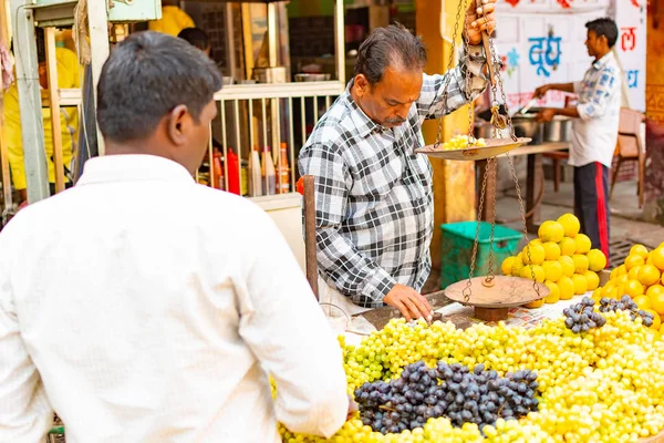 India, Varanasi, Mar 10 2019-niet-geïdentificeerde verkoper man verkoopt en weegt druiven op de traditionele straat voedselmarkt — Stockfoto