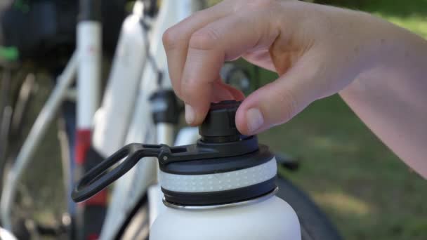 Hand takes black plastic cap from stainless steel insulated white bottle in new bicycle in background close-up 4K video — Stock Video