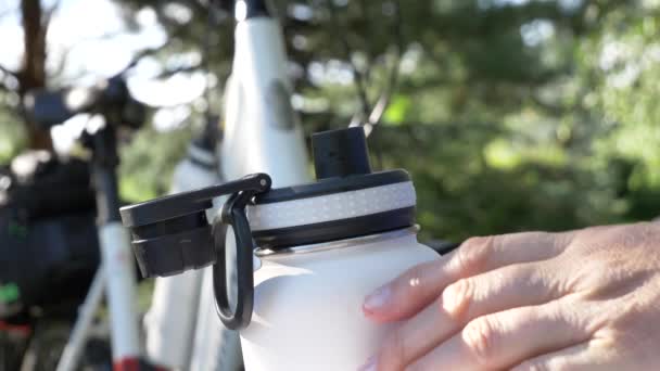 Hand nimmt schwarzen Plastikverschluss aus Edelstahl isolierte weiße Flasche in neuem Fahrrad im Hintergrund Nahaufnahme 4k Video — Stockvideo