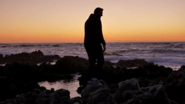 Erkek savaşçı keşiş gün batımında ya da gün doğumunda kayalık kayalıklarda Tai Chi karate kung fu pratik yapıyor. Kendini savunma sanatı. Pasifik sahilindeki dramatik destansı dalgaların arka planında siluet