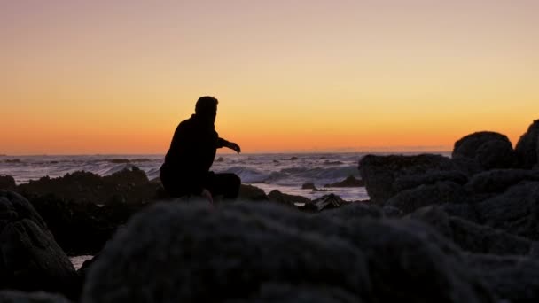 A férfiak lazítanak a sziklákon, nézik a naplementét a Csendes-óceán partján. — Stock videók