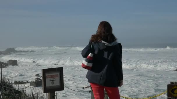 Woman standing in front of ocean trail closed high surf sign hughe waves — Stock Video