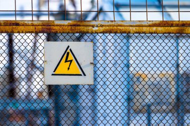 Yüksek elektrik voltaj tehlikeleri işaret uyarısı güç hattı Trafo Merkezi çevreleyen mesh çit asılı.