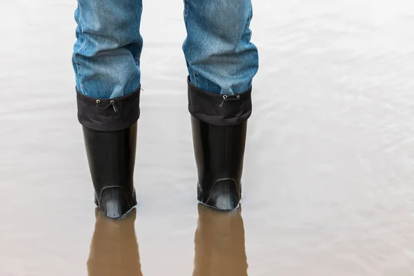 Man in rubber boots stands in a muddy puddle