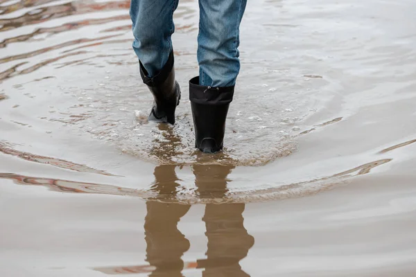 A man in rubber boots walks through a muddy puddle