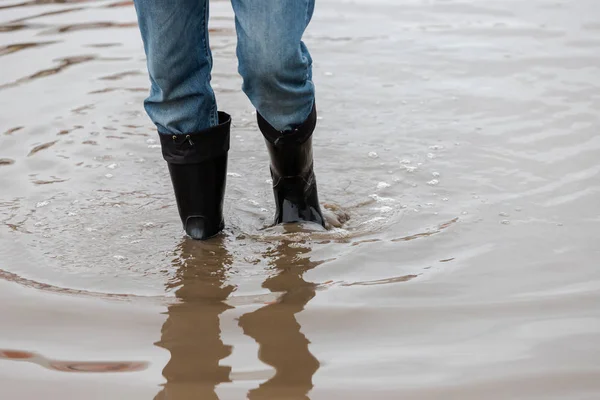 A man in rubber boots walks through a muddy puddle