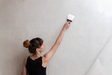 Kız dairenin onarımını yapar. Bir kadın beton duvara spatula açar. Dairenin tadilatı. Macun düzensizlikleri ve çatlaklar.