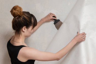 Kız beton duvar eski duvar kağıdı gözyaşları ve bir spatula tutar. Dairenin Renovasyonu.