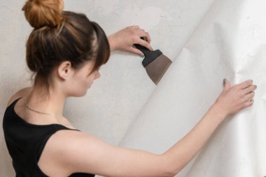 Kız beton duvar eski duvar kağıdı gözyaşları ve bir spatula tutar. Dairenin Renovasyonu.