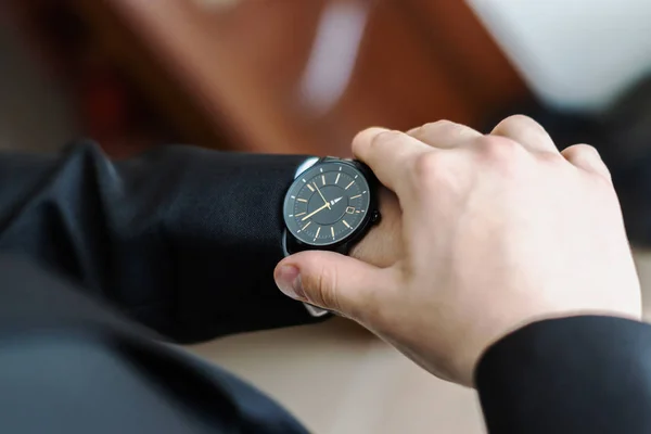 The groom looks at his watch to check the time. The watch is worn on the man's hand.