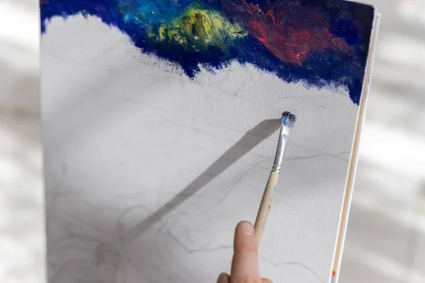 The girl artist paints a picture on canvas with oil paints. Close-up of the painting process.