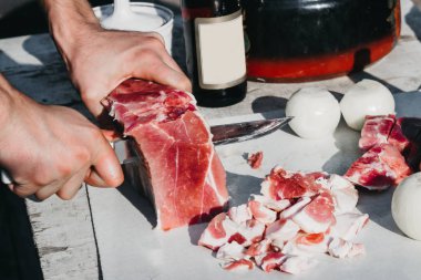 Turist büyük bir bıçakla bir parça et keser. Domuz pastırması ve soğan kebap pişirmek için. Tatillerde doğada yemek pişirmek..