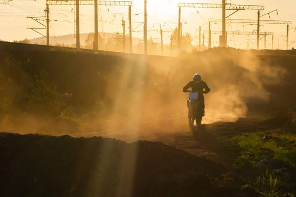 A man on a motocross bike rides along a dirt track. Off-road racing in the rays of the setting sun. Dust from the wheels.