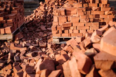 Kırık bir kırmızı bina tuğlası yığını yere saçıldı. Arka planda tuğlalar olan palet.