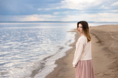 Genç ve güzel bir kız sahilde yürüyor ve arkasına bakıyor..