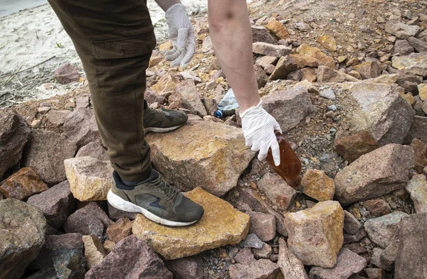 Genç adam, Kiev Denizi kıyısındaki sert plastik şişeler ve diğer çöplerle dolu kayalık sahildeki bir çöp torbasında plastik çöp topluyor. (Gönüllü konsept)