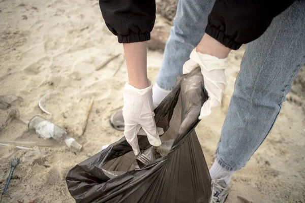 Genç bir kadın, Kiev Denizi kıyısındaki sert plastik şişeler ve diğer çöplerle dolu kumlu sahilde bir çöp torbasında plastik çöp topluyor. (Gönüllü konsept)