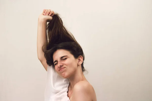 Bir şaka olarak saçlarını çeker çiller ile genç güzel kadının fotoğraf portresi kadar kapatın. Gri arka planda komik bir yüz. Hemşirelik saç bakımı