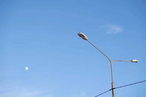 Street lamp and moon on a clear blue sky with light feathery clo