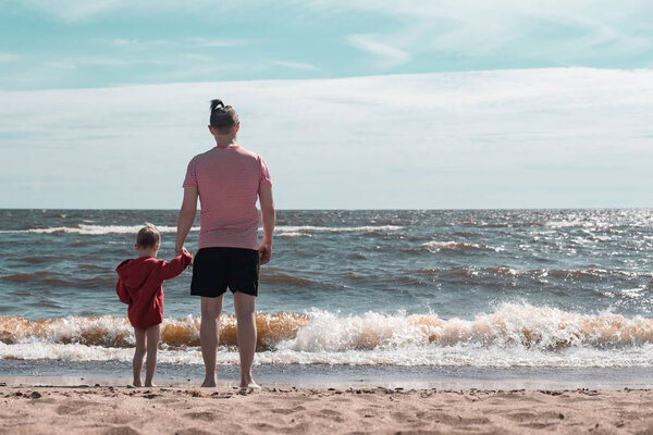 Папа и сын держатся за руки и смотрят на море. Дружба и любовь между ребенком и родителем
