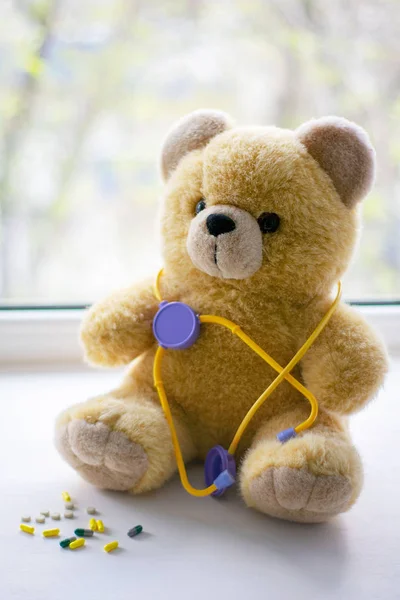 Urso de pelúcia bonito com um fonendoscópio ao lado de pílulas no conceito de saúde pediátrica — Fotografia de Stock