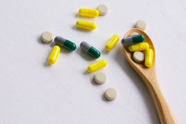 Tahta kaşıkta çeşitli ilaç hapları, tabletler ve kapsüller.