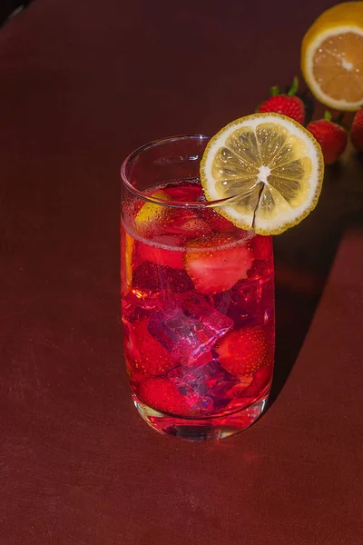 Beva con ghiaccio da fragole su uno sfondo scuro. Cocktail di fragole fresche. Cocktail estivo fresco con cubetti di fragola e ghiaccio. Bicchiere di bibita alla fragola su sfondo scuro . — Foto Stock