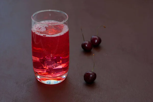 Beba con cerezas heladas, cerezas dulces sobre un fondo oscuro. Cóctel de ciruela fresca. Cóctel fresco de verano con cerezas y cubitos de hielo. Un vaso de refresco beber una cereza sobre un fondo oscuro . — Foto de Stock