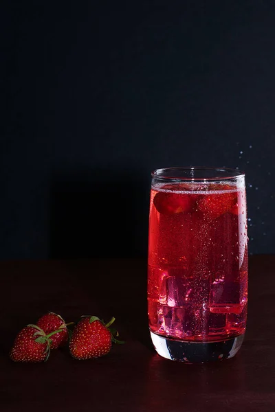 Beba com o gelo de morangos em um fundo escuro. Cocktail de morango fresco. Cocktail fresco de verão com cubos de morango e gelo. Copo de refrigerante de morango no fundo escuro . — Fotografia de Stock