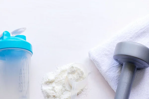 Protein shake, dumbbells and towel on white background