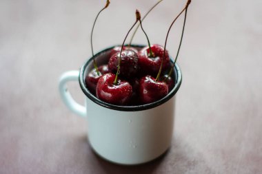 Koyu bir arka plan üzerinde beyaz metal kupa olgun kiraz meyveleri. Country stili