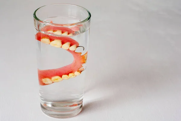 Οδοντοστοιχία σε ένα ποτήρι με νερό σε λευκό φόντο — Φωτογραφία Αρχείου