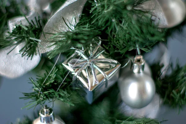 Juguete de árbol de Navidad en forma de caja de plata colgando de las ramas de un árbol de Navidad artificial —  Fotos de Stock