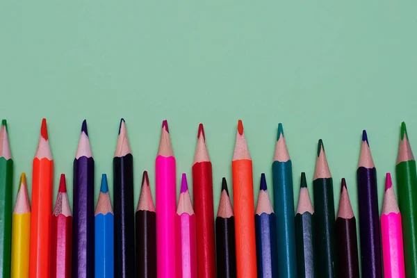 Many colored pencils lie on a green background. Copy spase. The concept of back to school, the educational process, study at school, drawing