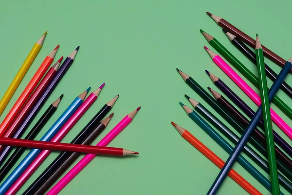 Many colored pencils lie on a green background. Copy spase. The concept of back to school, the educational process, study at school, drawing