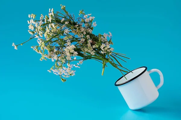Balancing white mug with white spring flowers splashing around on a blue background.