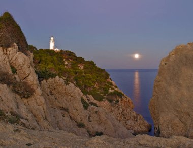 Lighthouse Far de capdepera, dusk, moonbeam on sea,rocks and trees, cala ratjada, mallorca, spain. clipart