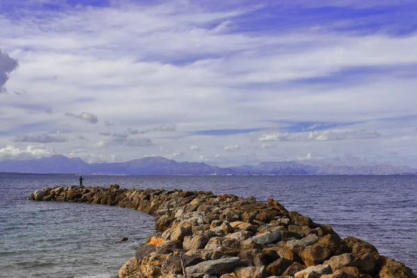 Jetty / pier of rocks with man fishing and mountain backdrop, mediterranean sea, mallorca, spain. — Stock Photo, Image