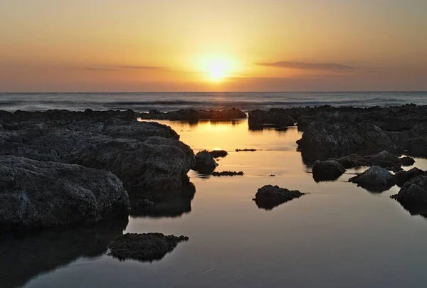 Nascer do sol sobre mediterrâneo, com céu dramático e piscinas rochosas refletindo raios solares em primeiro plano, cala bona, Maiorca, Espanha . — Fotografia de Stock