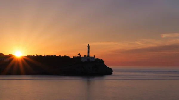 Portocolom lighthouse sunrise, silhouette, beautiful colourful sky, sun beams, calm sea, Mallorca, Spain.