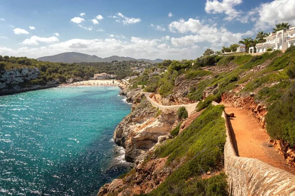 Tipik İspanyol sahili. Sahile giden patika yeşil tepeler ve mavi gökyüzü ile çevrili dağlar, Cala Romantica, Mallorcal, İspanya.