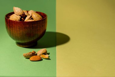 Yeşil ve sarı arka planda kabuğu olmayan bademlerin yanında bir kase çiğ badem.
